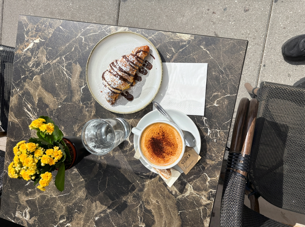 Cappuccino og croissant på et marmorbord i udeserveringen hos Cafe Katz